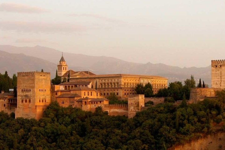 a castle with a clock on the tower of the city with Alhambra in the background