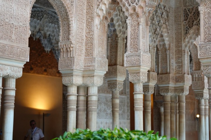 Ornate archways and columns with intricate designs, greenery in foreground.